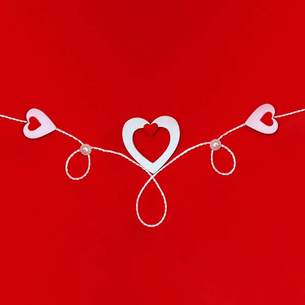 Draufsicht auf eine Komposition zum Valentinstag auf rotem Hintergrund mit weißen und roten Herzen und einem weißen Seil. Urlaubskonzept, Grußkarte, Hintergrund. — Stockfoto