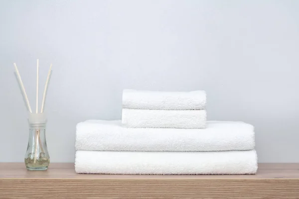 Banyodaki bir rafta düzgünce katlanmış beyaz havlular ve yanında da kokulu toplar ve tahta sopalarla dolu cam bir kavanoz var. Spa konsepti, evde düzen, tekstil.