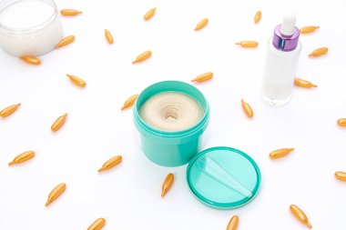 Parlak turkuaz bir krema kavanozunun üst görüntüsü, pembe bir cam şişe ve beyaz arka planda altın renkli kolajen kapsüller. Güzellik konsepti, yüz bakımı, kozmetoloji, tıp