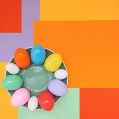 Paskalya yumurtalarının bir tabakta duran kompozisyonu ve modaya uygun bir renk şemasında simetrik olmayan parlak bir arka plan. Kavram geçmişi, tatil, paskalya, çocukların yaratıcılığı