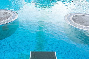 Top view of a diving board against the background of a pool with blue water in which a person swims. The concept of summer, relaxation, spa, aqua park, sports, architecture.