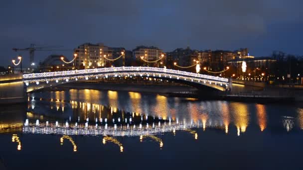 Utsikt över bron över floden i staden, dekorerad med ljus belysning och gatlyktor som återspeglas i vattnet på kvällen. Begreppet stad, jul, arkitektur, landskap. — Stockvideo