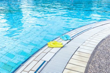 Havuzun kenarında duran sarı ve mavi parmak arası terliklerin görüntüsü. Yaz konsepti, tatil, spa, su parkı, seyahat