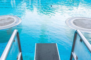 Top view close-up on a diving board against the background of a pool with blue water in which a person swims. The concept of summer, relaxation, spa, aqua park, sports, architecture