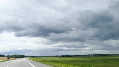 Beyaz Rusya 'da otoban boyunca uzanan bir arabanın ön camından vurularak gökyüzünün arka planında kalın bulutlar ve tarlalar oluşturuldu..