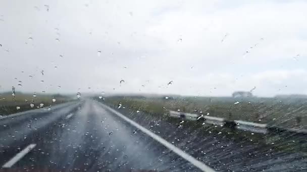 Strzał kropel deszczu, które spływają przez przednią szybę samochodu jadącego po autostradzie w deszczową pogodę.. — Wideo stockowe