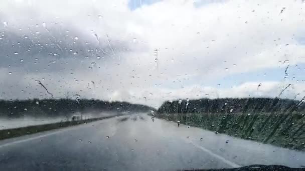 Yağmurlu bir havada otobanda giden bir arabanın ön camından akan yağmur damlaları.. — Stok video