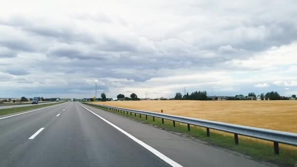 Un disparo a través del parabrisas de un coche que recorre la autopista de Bielorrusia contra el fondo del cielo con densas nubes y campos . — Vídeos de Stock