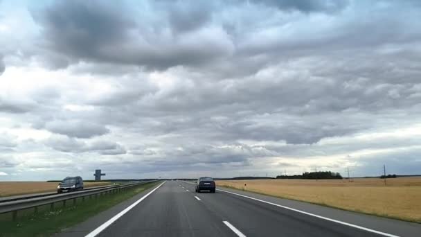 Bielorrusia. Vitebsk. 04.07.2019. Un disparo a través del parabrisas de un coche que recorre la autopista de Bielorrusia contra el fondo del cielo con densas nubes y campos . — Vídeos de Stock
