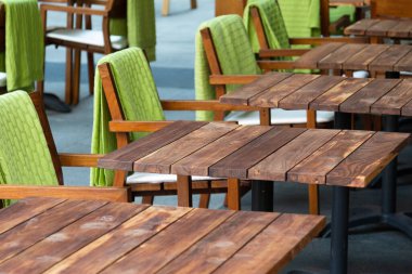 Yanında yeşil halıları olan sandalyelerin olduğu bir sokak kafesindeki boş ahşap masaların manzarası. Kavram şehri, kafe, yemek şirketi, kriz.