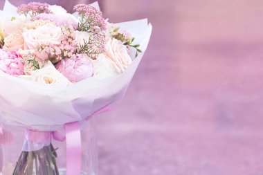 Pembe şakayık çiçekleri ve pembe arka plandaki cam bir vazoda duran beyaz kağıtta duran gülleri görmek. Kavram arkaplanı, çiçekler.