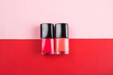 Kırmızı ve pembe arka planda izole edilmiş parlak tırnak cilası şişeleri.