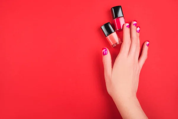 Kobieta Ręka Jasnym Manicure Lakier Paznokci Butelki Izolowane Czerwonym Tle — Zdjęcie stockowe