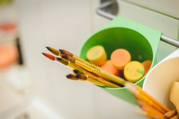 Resim atölyesinde çizim aletleri. Üstten açıyla, paletteki boya fırçalarının, yağlı boya fırçalarının fırça darbelerinin, büyük püsküllerin fotoğrafını göster.