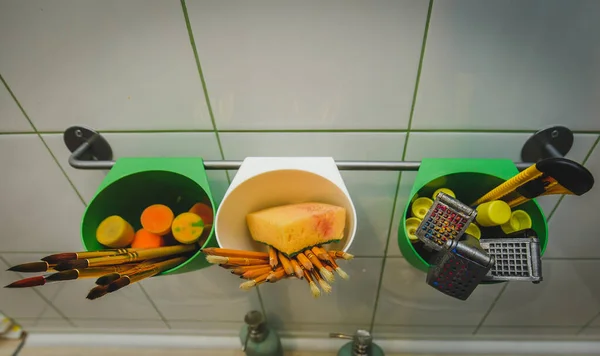 Resim atölyesinde çizim aletleri. Üstten açıyla, paletteki boya fırçalarının, yağlı boya fırçalarının fırça darbelerinin, büyük püsküllerin fotoğrafını göster.