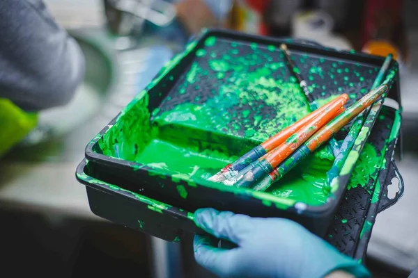 İçinde fırça olan yeşil boya dolu bir küvet. Okulda ya da anaokulunda ya da eğitim merkezinde sınıf dersleri. Atmosfer çizimi