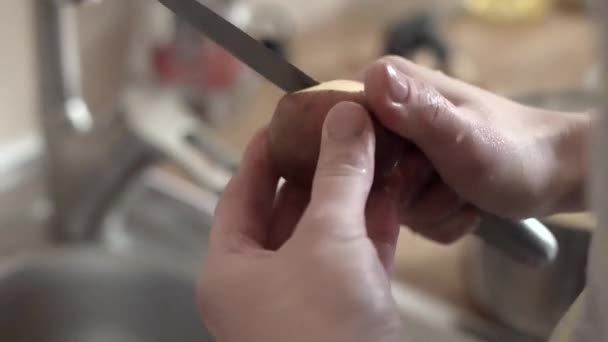 Женские руки чистят картошку на кухне — стоковое видео
