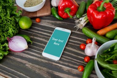 Taze organik sebze ve ahşap arka plan, dijital tarifi kitabı ve alışveriş listesi kavramı üzerinde Center'da smartphone.