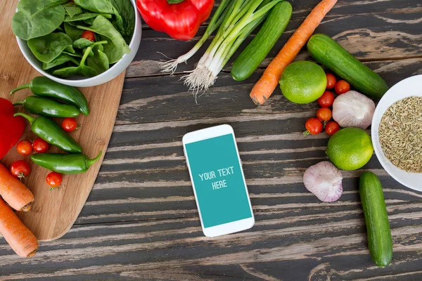 Свіжі органічні овочі та смартфон у центрі на дерев'яному фоні, концепція цифрової книги рецептів та списку покупок . — стокове фото