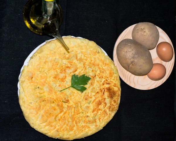 A spanish tortilla de patatas view from above with the ingredients: potatoes, eggs and olive oil — Stock Photo, Image