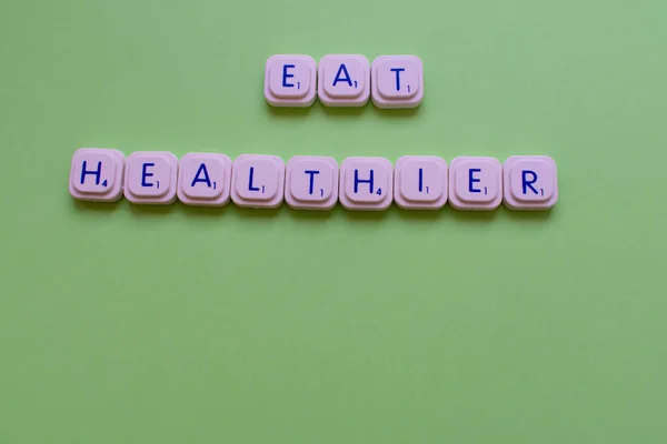 Motivational slogan: Eat healthier, over a green background made with playing letters