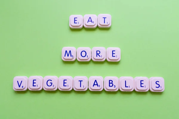 Motivational slogan: Eat more vegetables, over a green background made with playing letters
