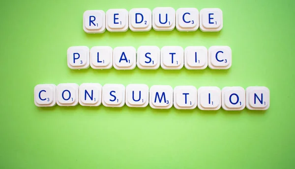 Mengurangi konsumsi plastik, pesan terhadap polusi plastik di atas latar belakang hijau yang dibuat dengan huruf bermain — Stok Foto