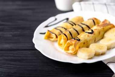 Siyah ahşap zemin üzerine muz çikolata şurubu ile Pancakes.