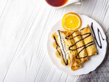 Krep muz ile beyaz ahşap zemin üzerinde çikolata şurubu ile süslenmiş krem şanti. Ve bir bardak çay