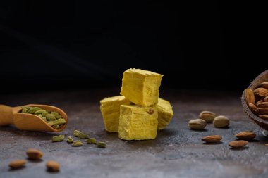 Soan papdi küp, tahta kepçe içinde kakule taneleri beton mutfak yüzeyinde fıstıklar ve badem ve siyah fotokopi alanı..