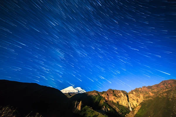 Hvězdy kreslení čar vyblednutí a mraky nad Mount Elbrus. Noční země — Stock fotografie