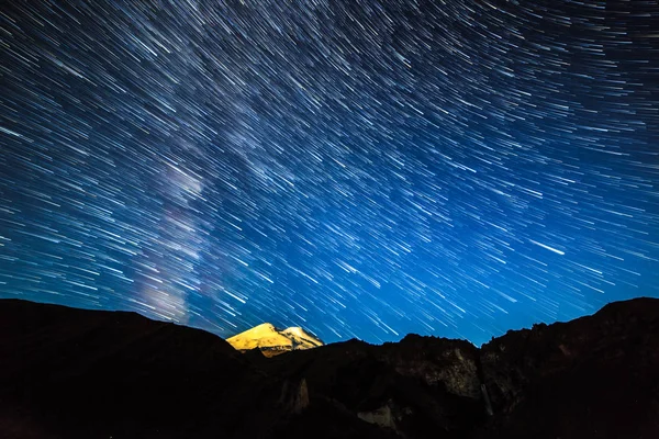 Hvězdy kreslení čar vyblednutí a mraky nad Mount Elbrus. Noční země — Stock fotografie