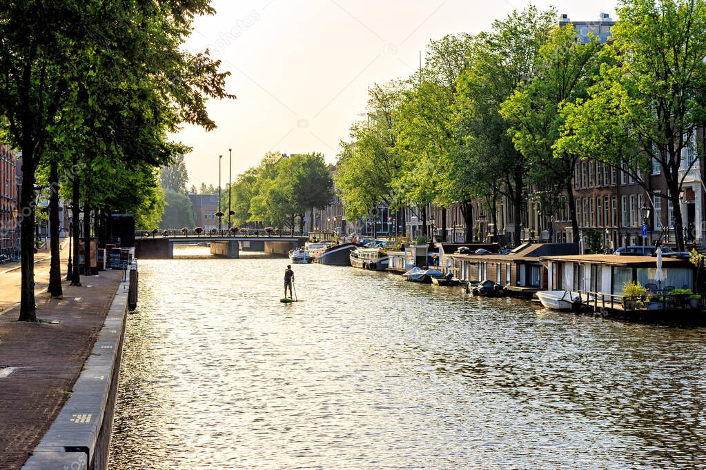 Amsterdam, Netherlands. A man is engaged in SUP (Stand Up Paddle). Residential barges and houses on the water. Canal (street) Nieuwe Keizersgracht. The historic city center