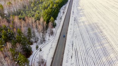 Mavi araba yolda geziyor. Tarlanın etrafında ve orman karla kaplı. Rusya, Ural, Hava Görünümü  