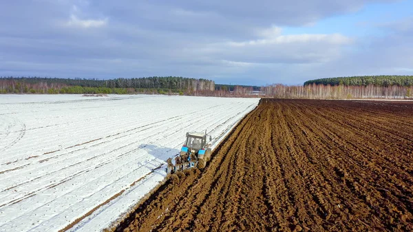 Egy Kék Traktor Felszántja Havas Mezőt Traktor Mögött Fekete Föld — Stock Fotó