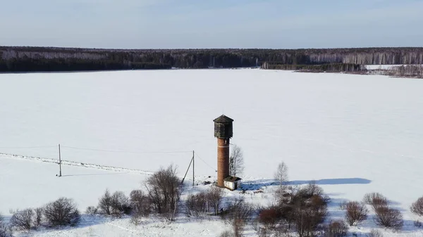 冬に空を飛ぶ 雪に覆われたフィールド上の古い水の塔 空中ビュー — ストック写真