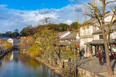 Okayama, Japonya - 30 Aralık 2018: Kurashiki Bikan Tarihi Bölgesi. Kurashiki Nehri 'nin kıyılarında söğüt ağaçları ve konutlardan oluşan Japon beyaz duvarlarıyla bilinen şehir manzarası