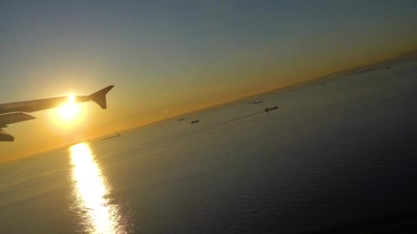日の出の時刻に東京羽田空港を離陸する航空会社 海の上に大きな明るい太陽の光 表面に黄金の反射 京浜工業地帯付近 Uhd — ストック動画
