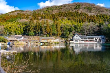 Yufuin, Oita Bölgesi, Japonya - 5 Ocak 2020: Kışın güneşli bir günde Altın Pul Gölü ve Yufu Dağı ve açık mavi gökyüzü. Bu popüler gezi yeri turistler tarafından sıklıkla izleniyor ve fotoğraflanıyor.