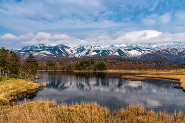 Güzel göl ayna gibi mavi gökyüzünü yansıtıyor, dönen dağ sıraları ve baharda güneşli bir günde arka planda ağaçlık alan. Yüksek enlem ülkesi doğal güzellik manzarası
