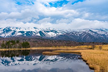 Güzel göl ayna gibi mavi gökyüzünü yansıtıyor, dönen dağ sıraları ve baharda güneşli bir günde arka planda ağaçlık alan. Yüksek enlem ülkesi doğal güzellik manzarası