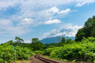 Arka planda Yotei Dağı 'nın olduğu bahar güneşli bir günde, Niseko Kasabası' nda Hakodate ana hattı demiryolu. Shiribeshi Eyaleti, Hokkaido, Japonya