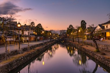 Okayama Bölgesi, Japonya - 27 Aralık 2019: Kurashiki Bikan Tarihi Bölgesi, alacakaranlıkta. Kentin tipik Japon yerleşim yerlerinin beyaz duvarları ve nehir kıyısında söğüt ağaçlarıyla bilinen manzarası.