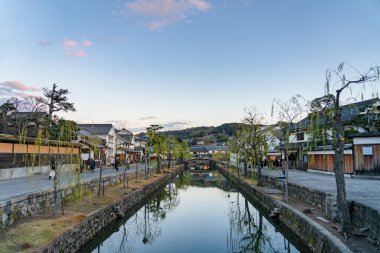 Okayama Bölgesi, Japonya - 27 Aralık 2019: Kurashiki Bikan Tarihi Bölgesi, alacakaranlıkta. Kentin tipik Japon yerleşim yerlerinin beyaz duvarları ve nehir kıyısında söğüt ağaçlarıyla bilinen manzarası.
