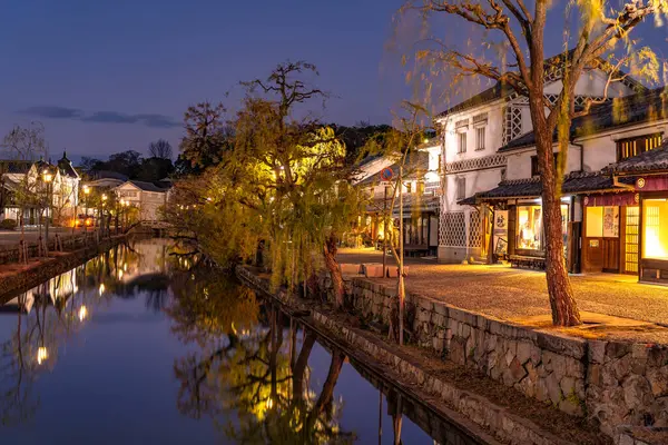 Okayama, Giappone - 27 dicembre 2019: Kurashiki Bikan Historical Quarter si illumina di notte. Paesaggio urbano noto per le tipiche pareti bianche giapponesi di residenze e salici che costeggiano le rive del fiume — Foto Stock