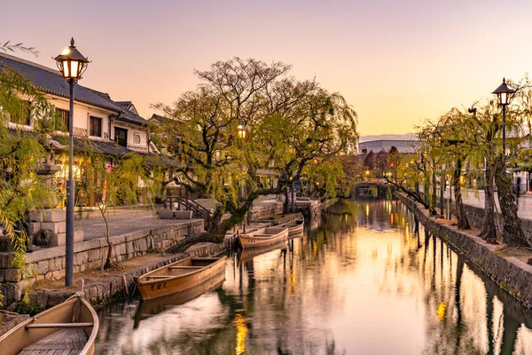 Okayama-Präfektur, Japan - 27. Dezember 2019: Das historische Viertel Kurashiki Bikan in der Abenddämmerung. Stadtbild, das für seine typisch japanischen weißen Häuserwände und Weiden am Ufer des Flusses bekannt ist — Stockfoto