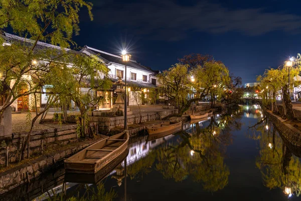 Okayama, Giappone - 27 dicembre 2019: Kurashiki Bikan Historical Quarter si illumina di notte. Paesaggio urbano noto per le tipiche pareti bianche giapponesi di residenze e salici che costeggiano le rive del fiume — Foto Stock