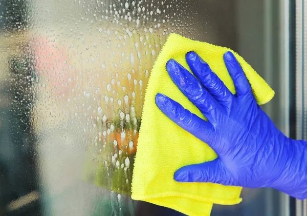 Mujer limpiando una ventana con un paño amarillo. — Foto de Stock