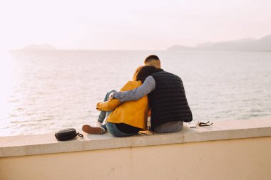 Genç çift yan yana oturmak ve denize doğru bakın. Genç günbatımı için bekleyin