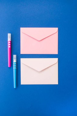Kopyalama alanı olan klasik mavi arkaplanda iki adet pembe ve beyaz zarf ve işaretleyici.